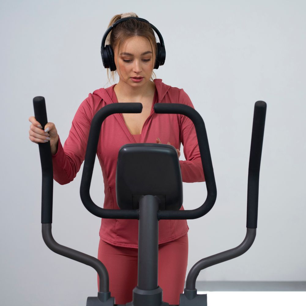 Woman exercising on a cross trainer with headphones on a light gray background